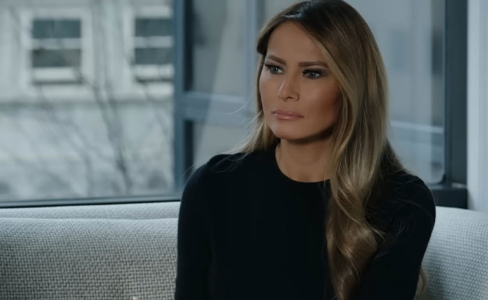 Melania Trump sitting on a couch indoors with a serious expression in her new documentary interview. Melania Trump sitting on a couch indoors with a serious expression in her new documentary interview.