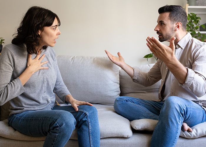 Wife and husband having a heated argument on a sofa, highlighting relationship troubles and reputation damage.