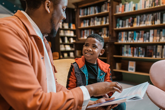 Father and son reading a book together in a library, highlighting a mom furious over teacher's inappropriate note controversy. Father and son reading a book together in a library, highlighting a mom furious over teacher's inappropriate note controversy.