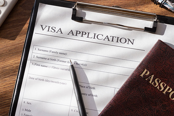 Visa application form on clipboard with pen and passport, related to mother-in-law stories and travel issues.