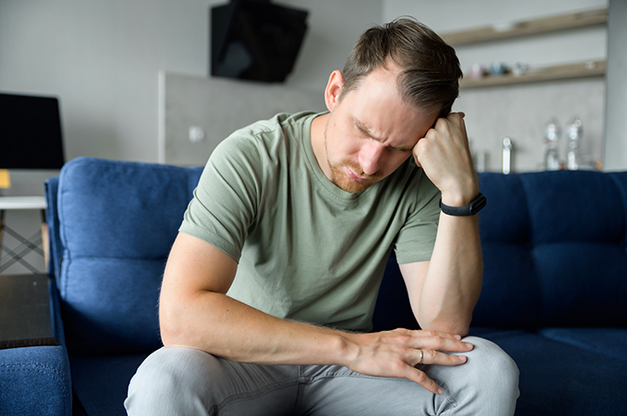 Man sitting on couch looking distressed, representing family tension and transphobic issues after son's coming out.