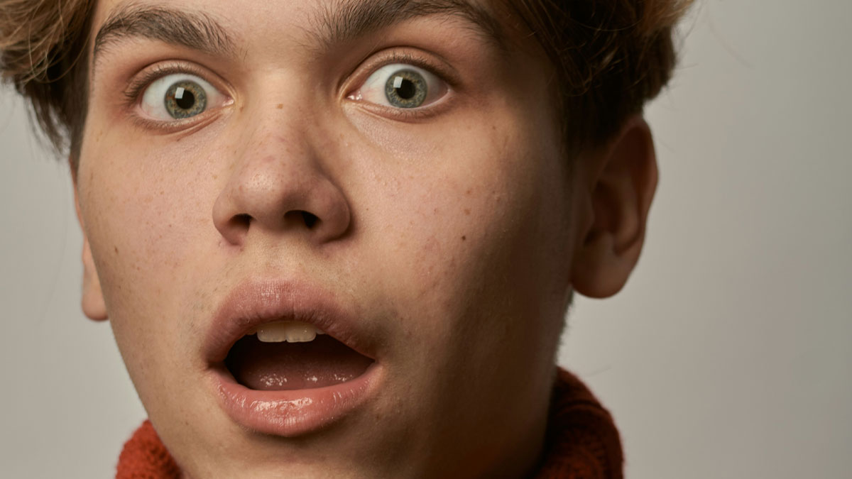 Close-up of a shocked young person with wide eyes and open mouth, questioning what they really saw.