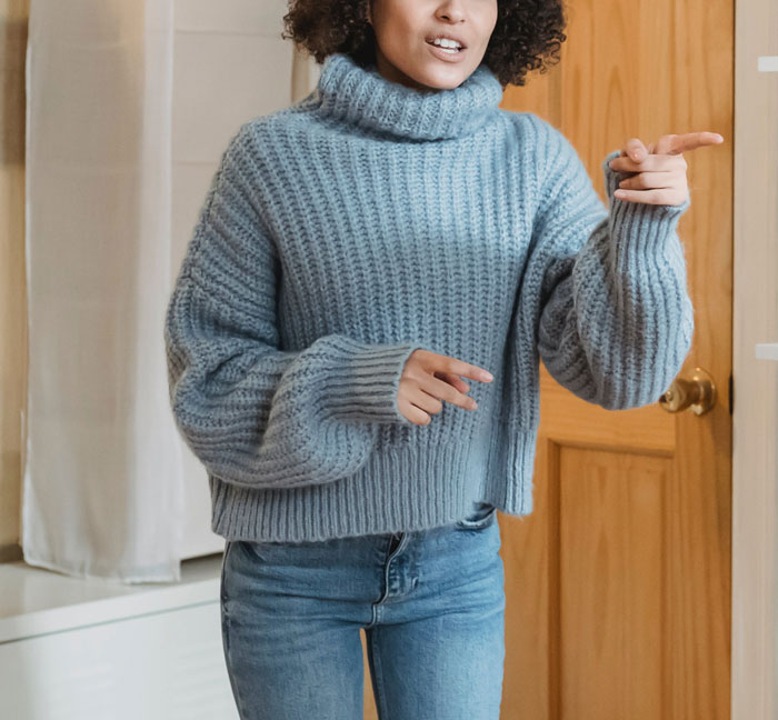 Woman in blue sweater gesturing angrily indoors, reflecting tension related to detangling daughter's friend's hair conflict.
