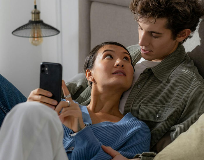 Woman showing proof of cheating on phone to her husband while sitting closely on couch at home. Woman showing proof of cheating on phone to her husband while sitting closely on couch at home.