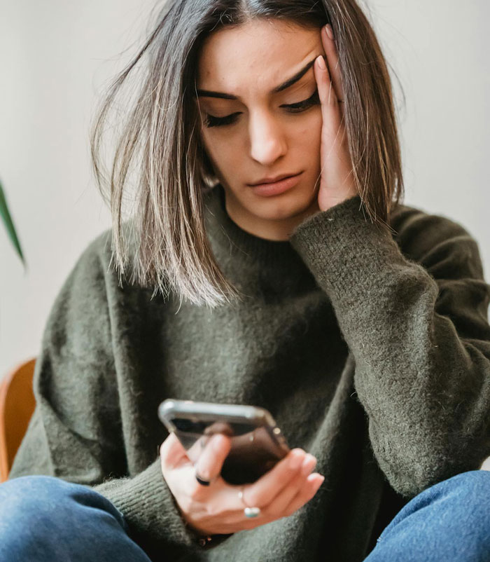 Woman with worried expression holding phone, representing proof her husband is cheating and dealing with crazy ex-girlfriends.