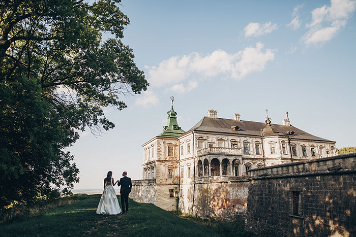 Bride and groom walking near a historic mansion, illustrating future in-laws' demand for prenup amid wealthy family background. Bride and groom walking near a historic mansion, illustrating future in-laws' demand for prenup amid wealthy family background.