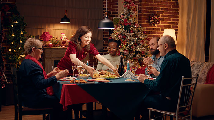 Woman bending over backwards serving food at holiday dinner, looking happy while others sit around the table. Woman bending over backwards serving food at holiday dinner, looking happy while others sit around the table.