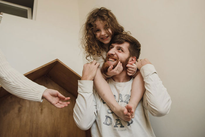 Man happily carrying stepdaughter on shoulders while woman reaches out, reflecting family tension and stepdaughter behavior issues. Man happily carrying stepdaughter on shoulders while woman reaches out, reflecting family tension and stepdaughter behavior issues.