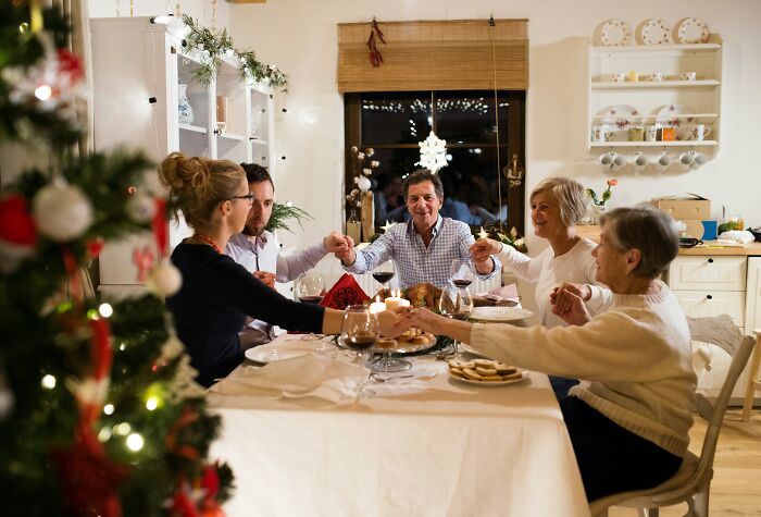 Family holding hands around a holiday dinner table, highlighting vegan teen&rsquo;s diet and family tension.