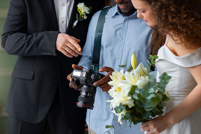 Bride and groom reviewing wedding photos with photographer, bride holding white lily bouquet, wedding day preparations. Bride and groom reviewing wedding photos with photographer, bride holding white lily bouquet, wedding day preparations.