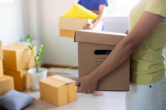 Woman holding a moving box inside a home filled with packed boxes, relating to secret texts and wedding photo worries. Woman holding a moving box inside a home filled with packed boxes, relating to secret texts and wedding photo worries.