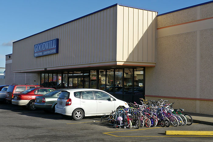 Goodwill store exterior with parked cars and bicycles, setting for older man and younger generations discussion. Goodwill store exterior with parked cars and bicycles, setting for older man and younger generations discussion.