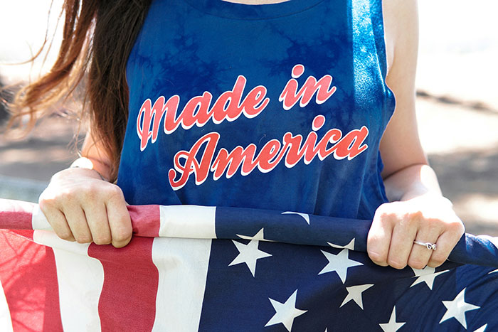 Woman wearing made in America tank top holding folded American flag outdoors on a sunny day Woman wearing made in America tank top holding folded American flag outdoors on a sunny day