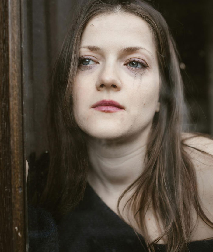 Woman with smudged makeup looking out a window, reflecting on uncertain affair partner's baby and complex family ties. Woman with smudged makeup looking out a window, reflecting on uncertain affair partner's baby and complex family ties.