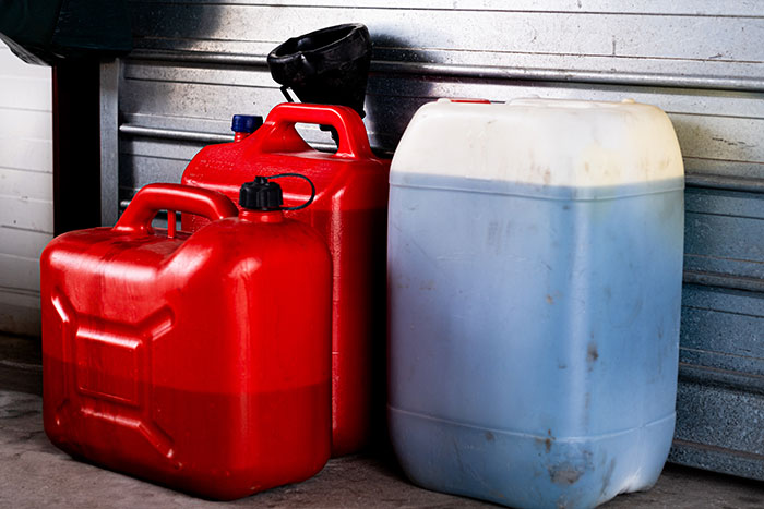 Gas cans and funnel by garage door illustrating mentally unstable woman attempting gas in drink incident