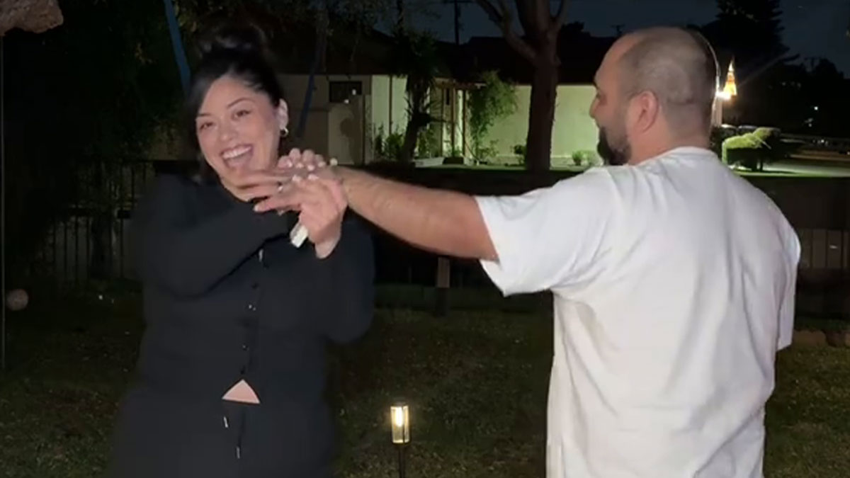 Woman smiling and showing a ring on her finger after a proposal to her boyfriend of 14 years outdoors at night.