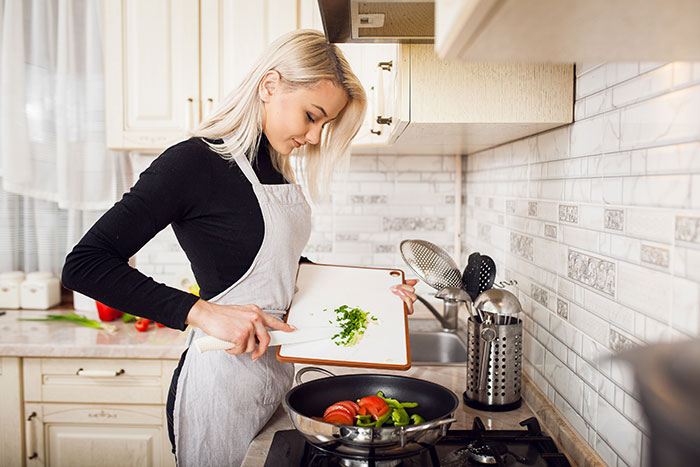 Young woman in apron cooking vegetables in kitchen, illustrating traditional wives concept in a modern setting. Young woman in apron cooking vegetables in kitchen, illustrating traditional wives concept in a modern setting.