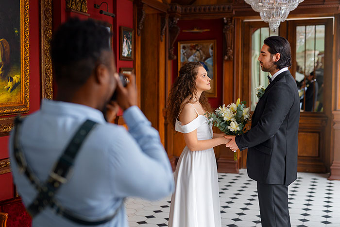 Bride and groom standing together while a photographer captures wedding photos in an elegant room with red walls. Bride and groom standing together while a photographer captures wedding photos in an elegant room with red walls.