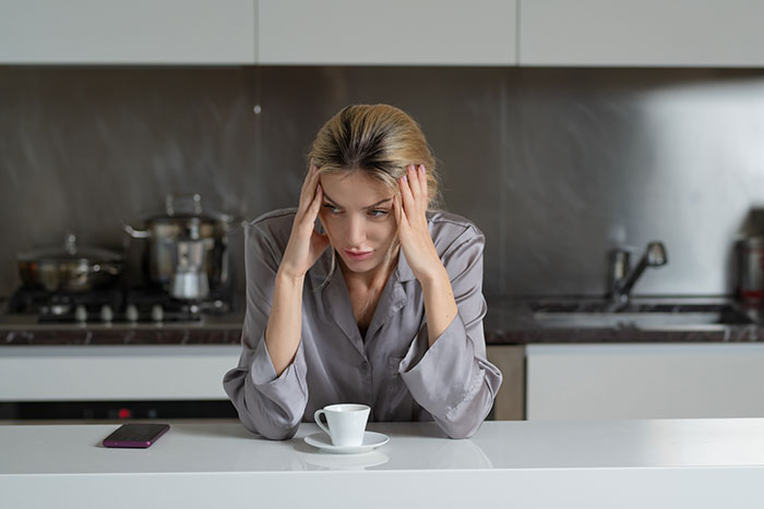 Single woman sitting in kitchen looking tired and stressed, reflecting on patterns men in relationships follow.