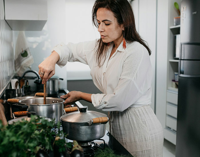 Woman cooking in kitchen stirring pots on stove preparing cooked lunches with focused expression Woman cooking in kitchen stirring pots on stove preparing cooked lunches with focused expression