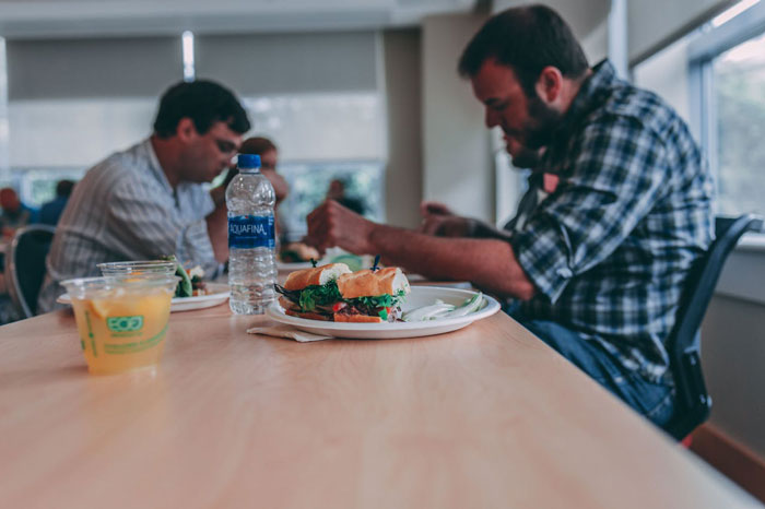 Man upset at lunch table with cooked sandwiches while others eat, reflecting woman upset boyfriend throwing away cooked lunches. Man upset at lunch table with cooked sandwiches while others eat, reflecting woman upset boyfriend throwing away cooked lunches.