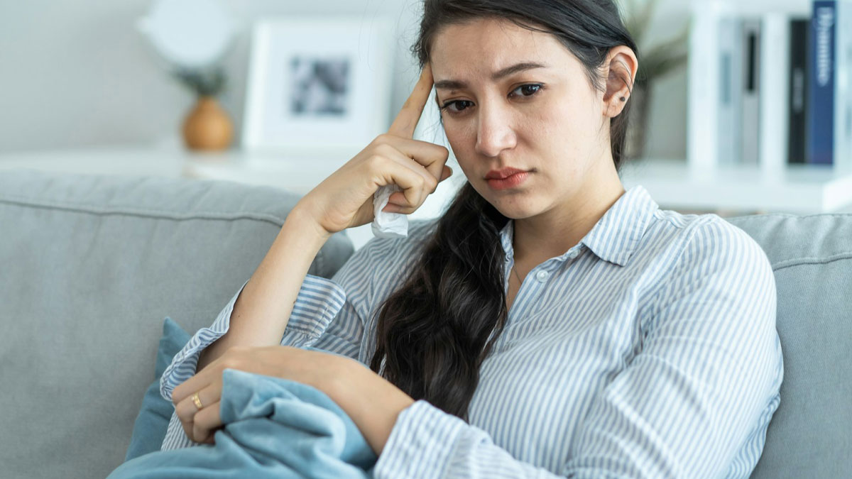 Upset woman sitting on sofa looking thoughtful and holding a tissue after boyfriend threw away cooked lunches.