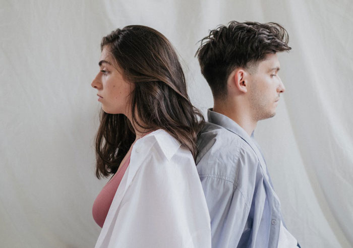 Young woman and man sitting back to back, highlighting family tension as woman doesn’t see daughter’s efforts. Young woman and man sitting back to back, highlighting family tension as woman doesn’t see daughter’s efforts.
