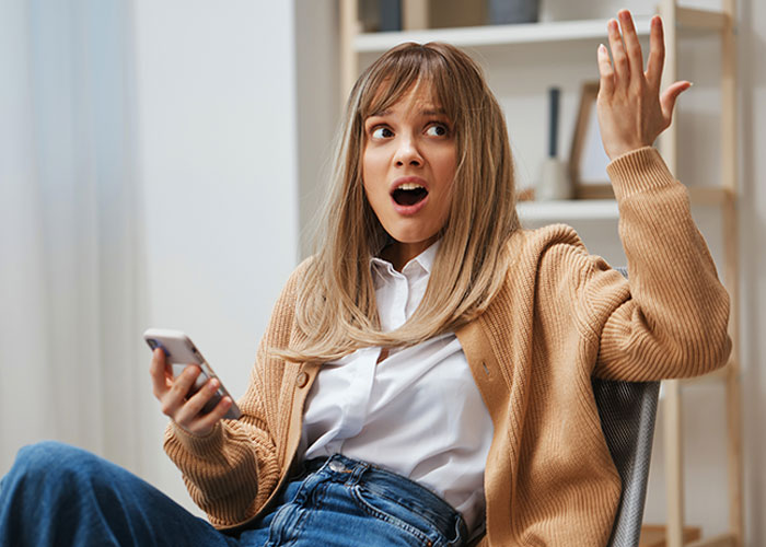 Young woman holding phone looking shocked and frustrated, illustrating makeup artist drama on wedding day for easy money scheme