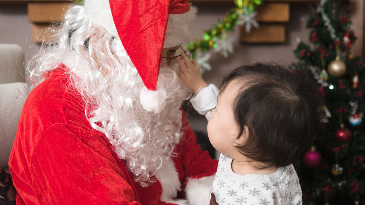 Baby touching Santa's glasses during a holiday visit, capturing a special moment between Santa and the child.