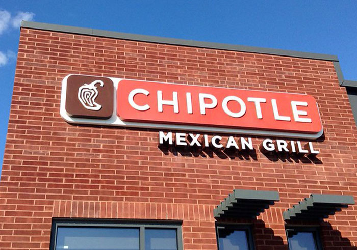 Chipotle Mexican Grill exterior sign on a brick building under a clear blue sky. Chipotle Mexican Grill exterior sign on a brick building under a clear blue sky.