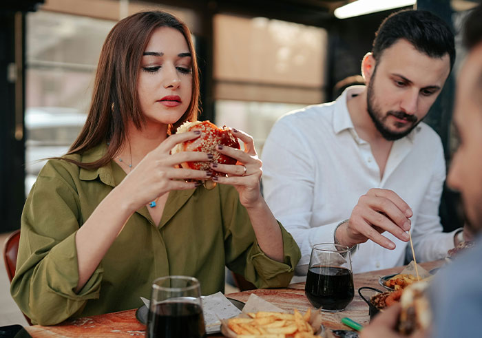 Woman holding a burger at a table with friends, testing if Chipotle adds more food to orders under male names. Woman holding a burger at a table with friends, testing if Chipotle adds more food to orders under male names.