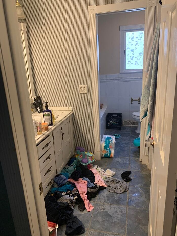 Messy bathroom with clothes scattered on floor and toiletries on the counter seen by home service professionals.