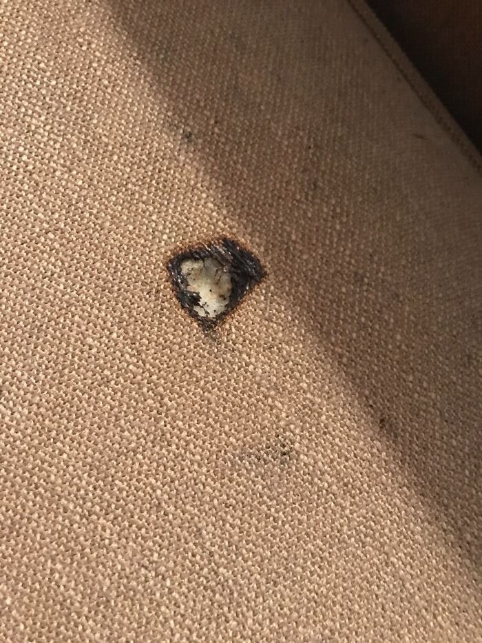 Close-up of a burn hole on beige fabric revealing startling damage seen by home service professionals.