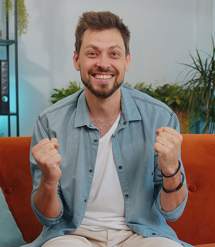 Happy man sitting on a couch with clenched fists, representing brands making mistakes and facing boycotts.