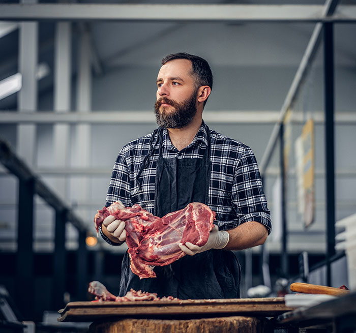 Man wearing gloves and apron holding raw meat in a butcher shop, illustrating brand mistake leading to customer boycott.