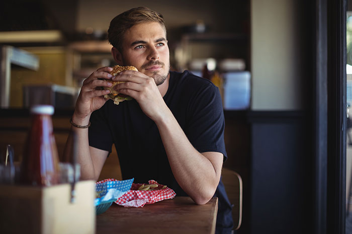 Young man eating a burger in a restaurant, illustrating brand mistake frustrations that led to customer boycotts.
