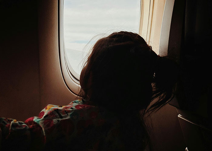 Child with hair tied looking out airplane window inside cabin, representing entitled person behavior in 2025 context.