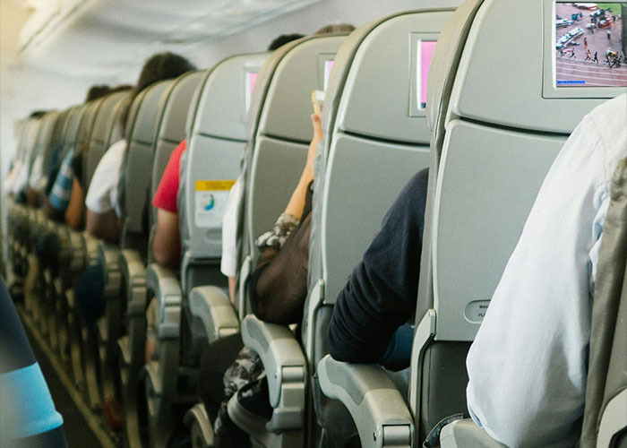 Passengers sitting in airplane economy seats with personal screens, illustrating entitled behavior in crowded travel settings.