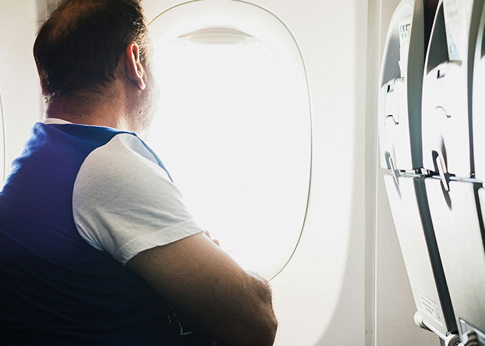 Man with crossed arms looking out airplane window, illustrating entitled person concept for 2025 awards article.