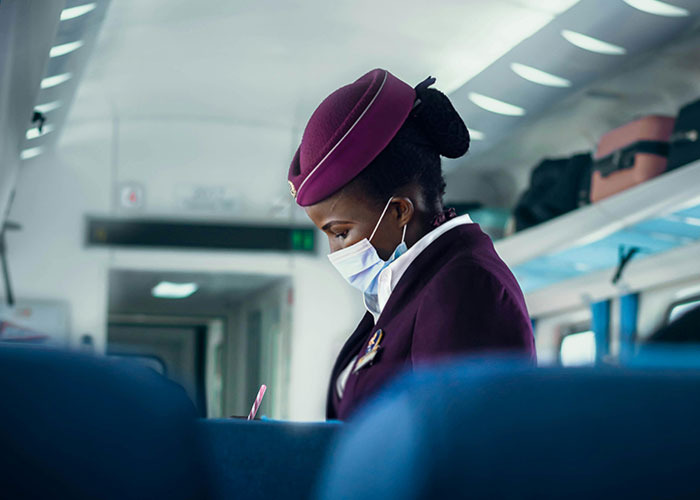 Flight attendant wearing a mask and uniform working inside an airplane, representing entitled person scenarios in 2025.