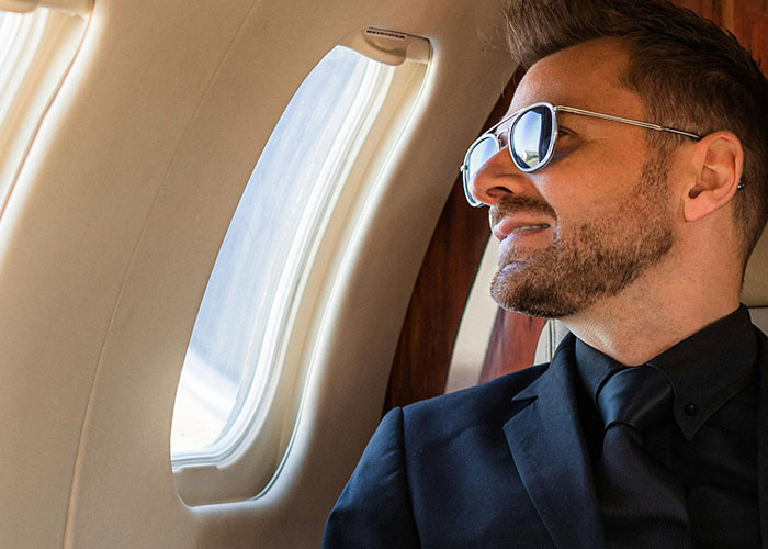 Man in sunglasses and suit sitting by an airplane window, exemplifying entitled person in 2025 concept.