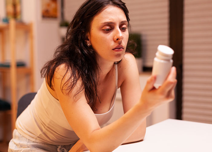 Young woman looking at a bottle of pills with a concerned expression, relating to a gym membership gift idea.