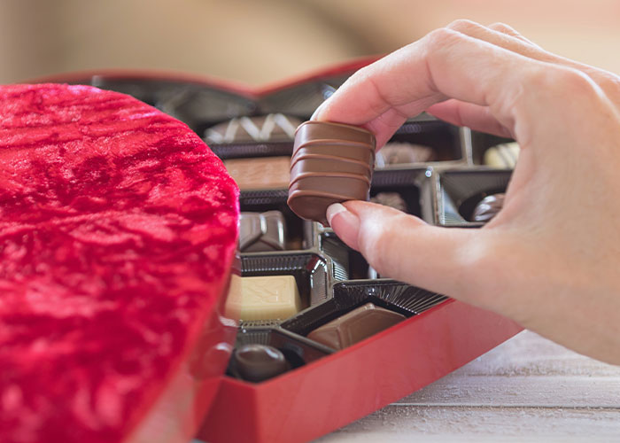 Hand picking chocolate from a heart-shaped box, symbolizing contrast to a gym membership gift in sensitive presents context.