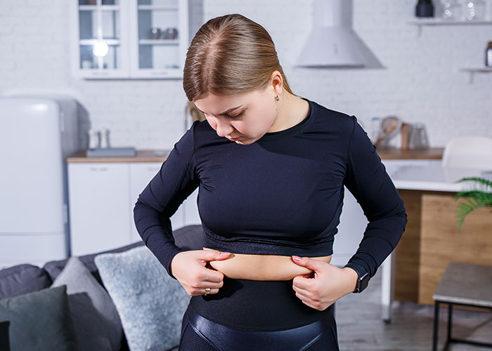 Young woman in workout clothes examining her stomach at home, illustrating reaction to a gym membership gift.