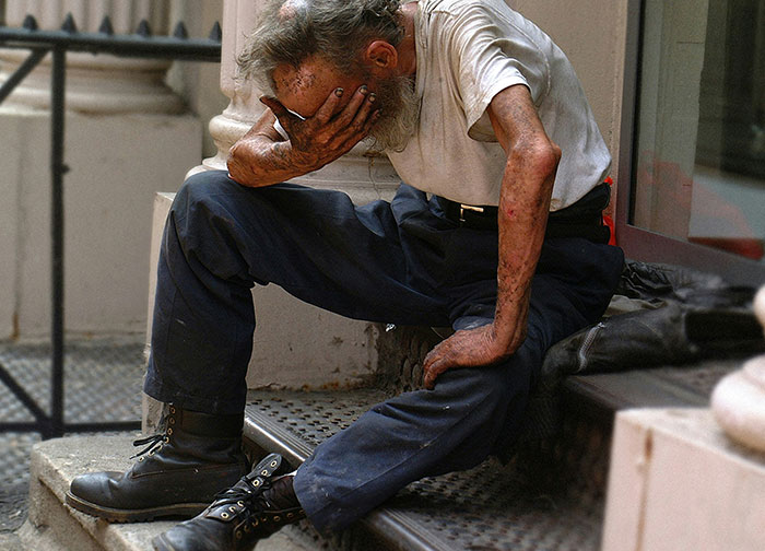Elderly man with visible skin wounds sitting on steps, appearing distressed, illustrating worst things patients endure in hospitals.