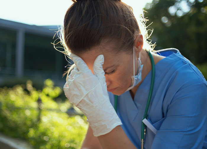 Healthcare worker in scrubs and gloves looking stressed outdoors, reflecting the worst things patients had to go through.
