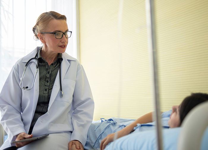 Female doctor in white coat with stethoscope talking to patient in hospital bed about worst things patients experience.