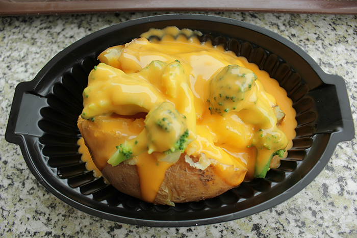 Baked potato covered with melted cheese and broccoli in a black plastic container, showing a unique eating style Baked potato covered with melted cheese and broccoli in a black plastic container, showing a unique eating style