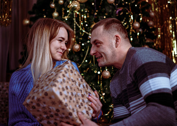 Couple exchanging holiday gift by Christmas tree, highlighting relationship and partner gift insights from expert warning. Couple exchanging holiday gift by Christmas tree, highlighting relationship and partner gift insights from expert warning.