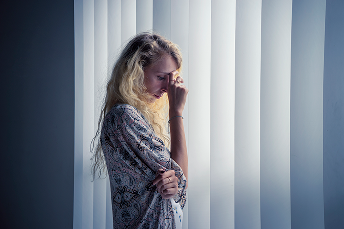 Bride standing alone in front of blinds, upset after overhearing groom's unexpected revelations at altar split.